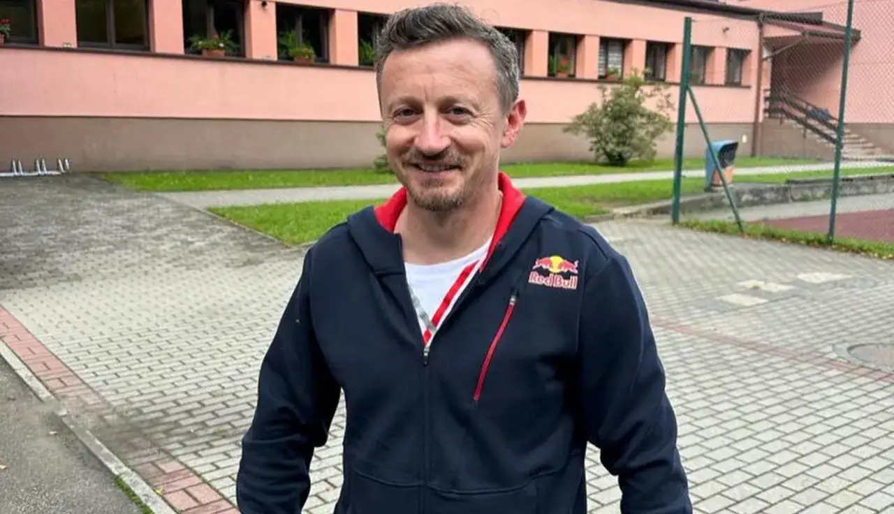 Adam Małysz w bluzie Red Bull, symbol jego sportowych sukcesów i budowania majątku. Uśmiechnięty przed budynkiem.