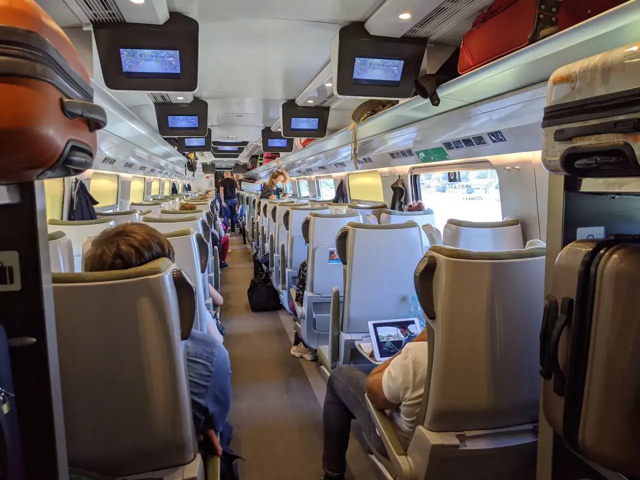 Wnętrze Pendolino, widok na rozkład miejsc. Pasażerowie podróżują, niektórzy oglądają filmy na tabletach.