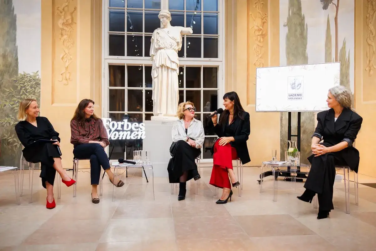Kobieta sigma w czerwonych spodniach i czarnej marynarce przemawia na panelu Forbes Women. Obok niej siedzą inne kobiety.