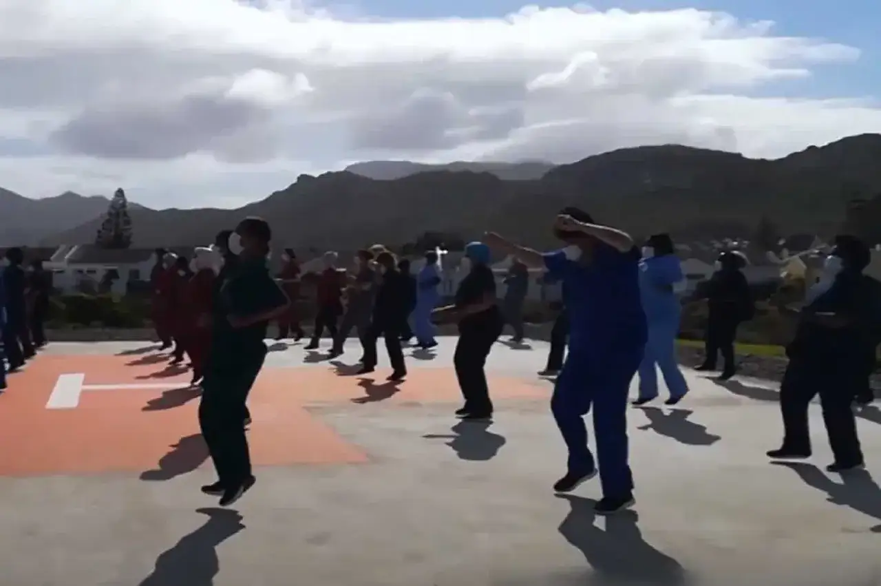 Grupa os&oacute;b w strojach medycznych uczy się tańca Jerusalem na zewnątrz.