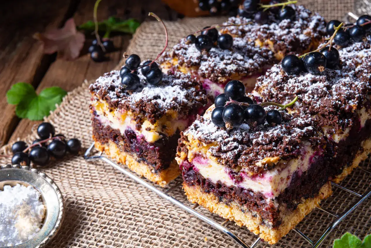 Pyszne ciasto pleśniak z dżemem porzeczkowym, posypane cukrem pudrem i świeżymi owocami. Idealne na deser.