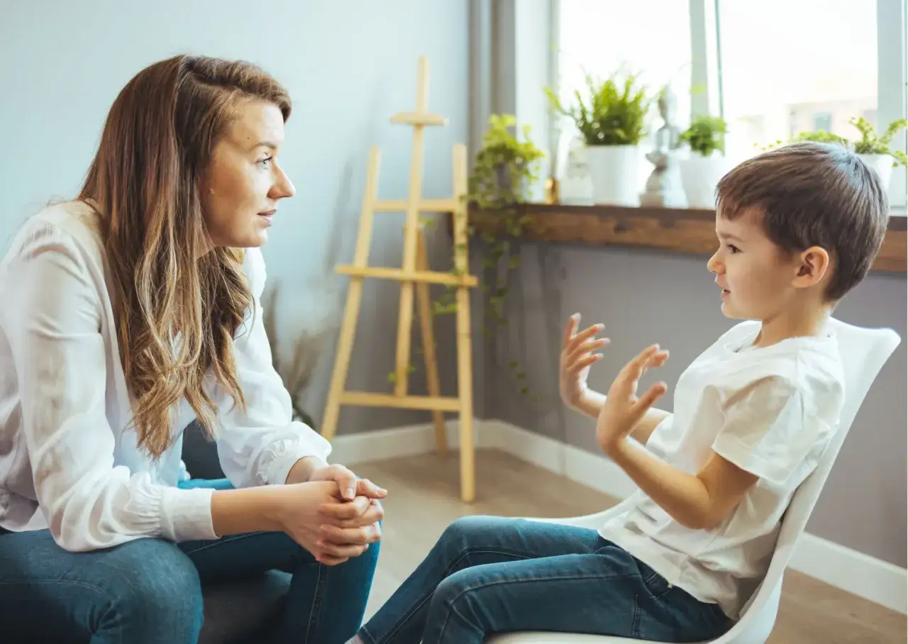 Matka spokojnie rozmawia z synem, ucząc go, jak rozmawiać z dzieckiem o złym zachowaniu. Dziecko gestykuluje, opowiadając o swoich emocjach.