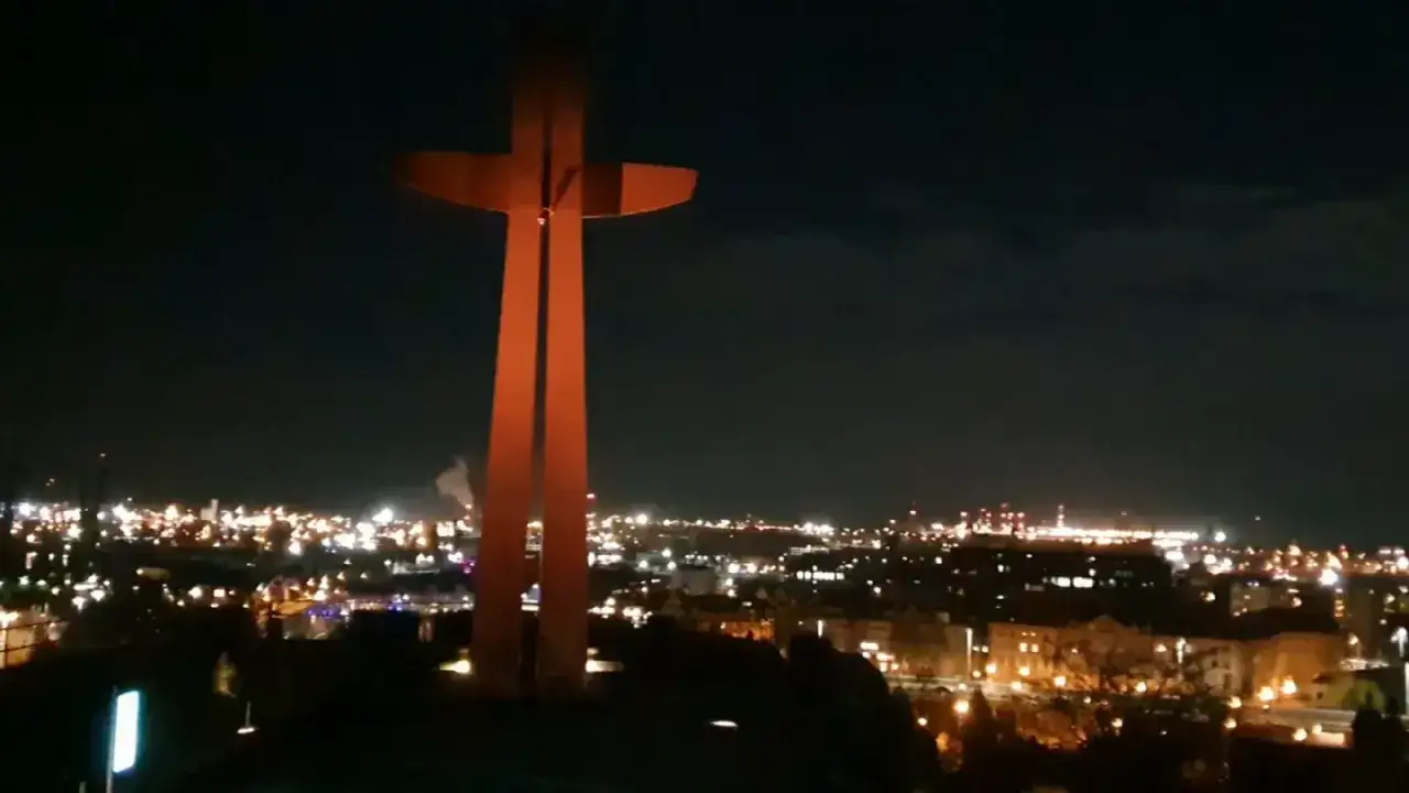 Wielki, pomarańczowy krzyż góruje nad nocnym miastem. To góra gradowa, która nocą rozświetla panoramę.