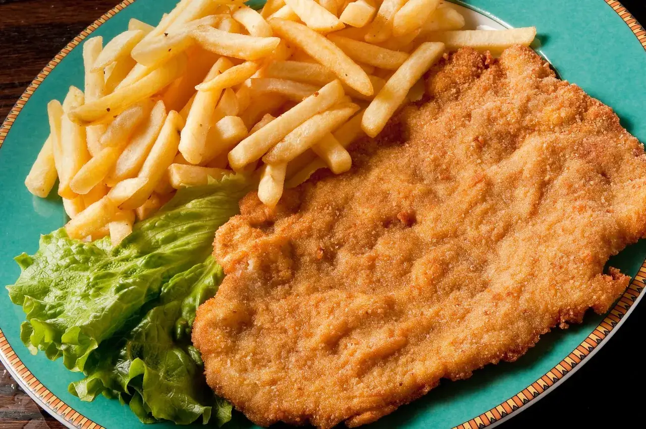 Złocisty sznycel cielęcy i kotlet schabowy z frytkami i sałatą na talerzu.