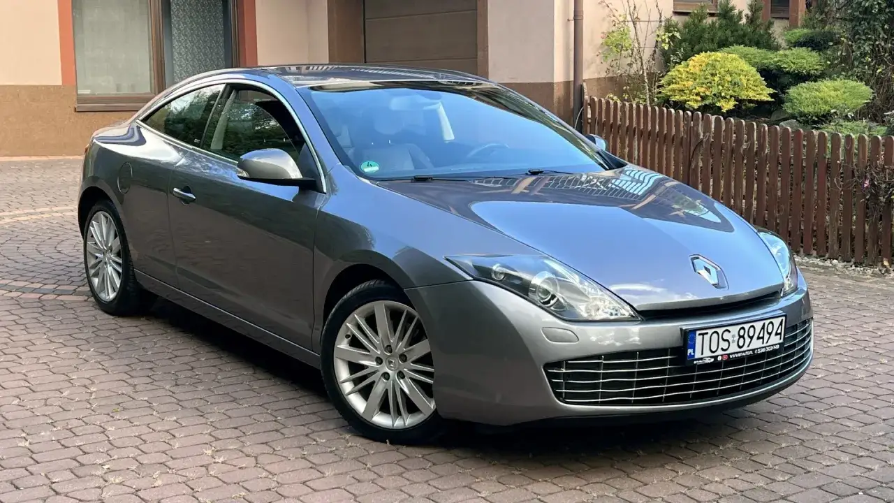Eleganckie, szare coupe Renault Laguna 3 stoi na brukowanym podjeździe, gotowe do podróży.