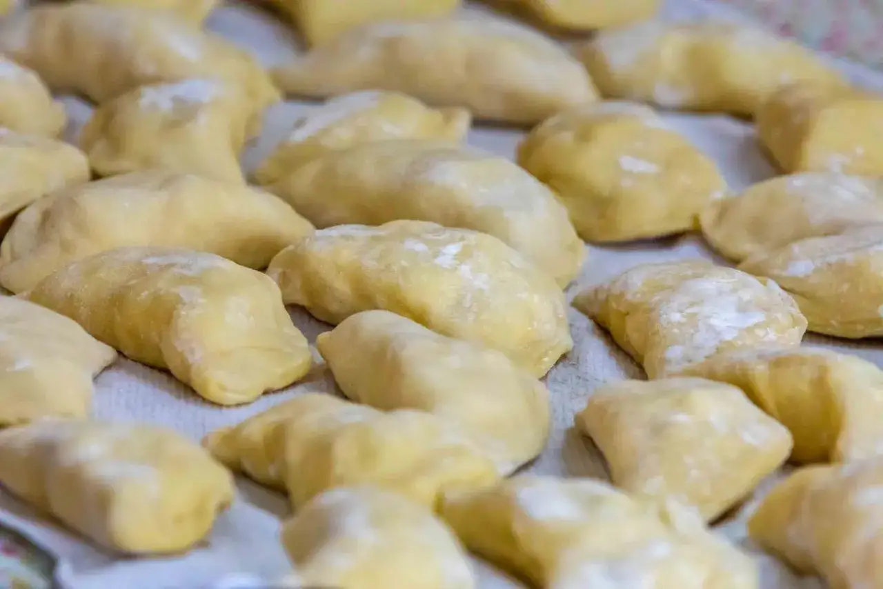 Gotowe do lepienia ciasto na pierogi, ułożone rzędami na białym obrusie, posypane mąką.