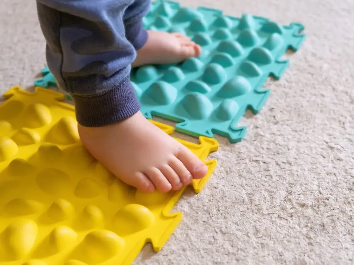 Dziecko stąpa po kolorowych matach sensorycznych, co jest jednym ze sposobów, jak leczyc zaburzenia sensoryczne.