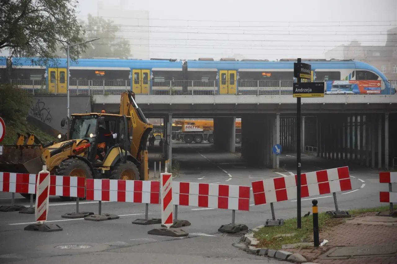 Prace drogowe w Katowicach: koparka, pociąg nad wiaduktem i znaki informacyjne.