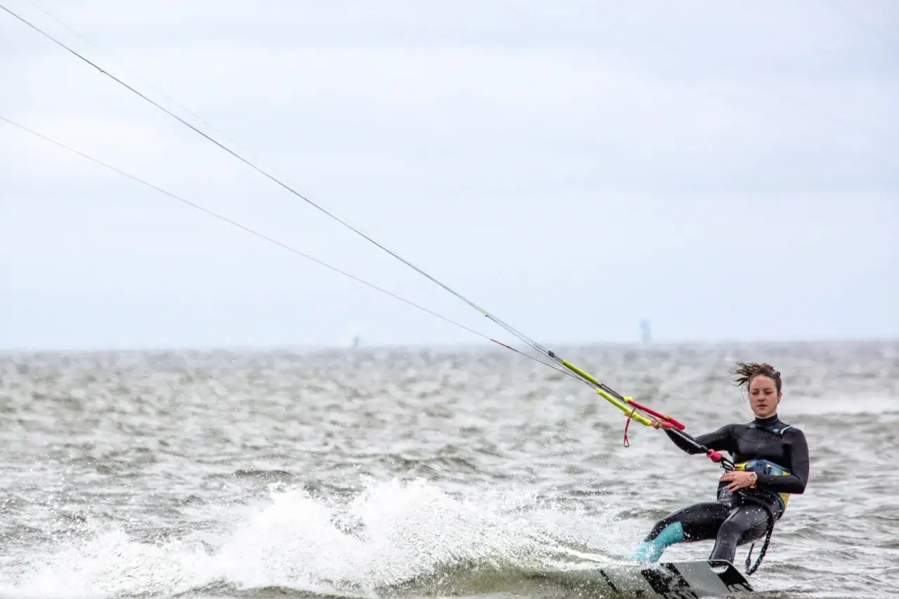 Kitesurfing Polska: młoda kobieta w piance ślizga się po falach, kontrolując latawiec.