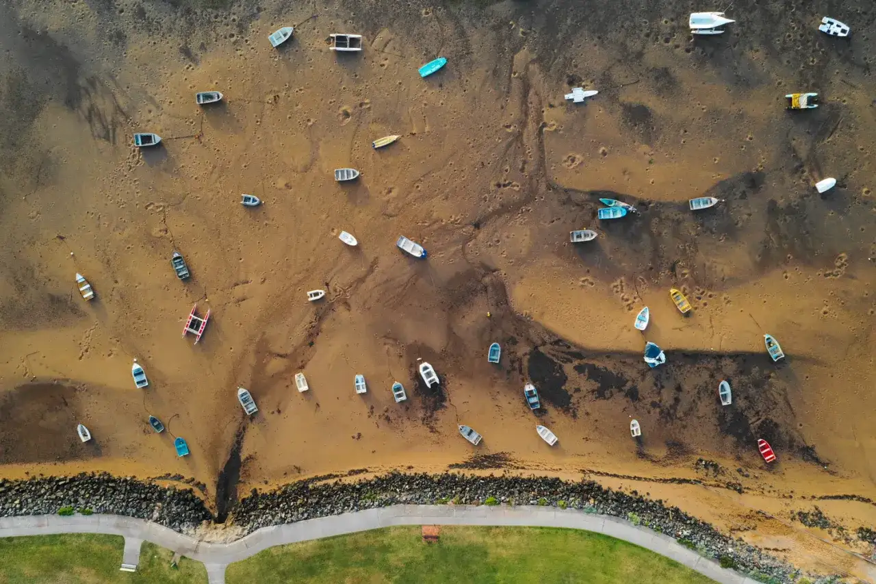 Zdjecia z drona ukazują plażę z licznymi łodziami na piasku po odpływie.