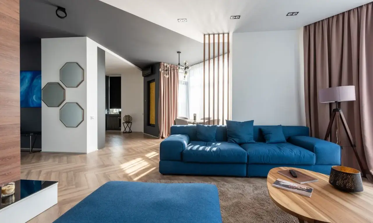 Nowoczesne mieszkanie w bloku z dużą, niebieską kanapą, drewnianą podłogą i ozdobnymi lustrami.