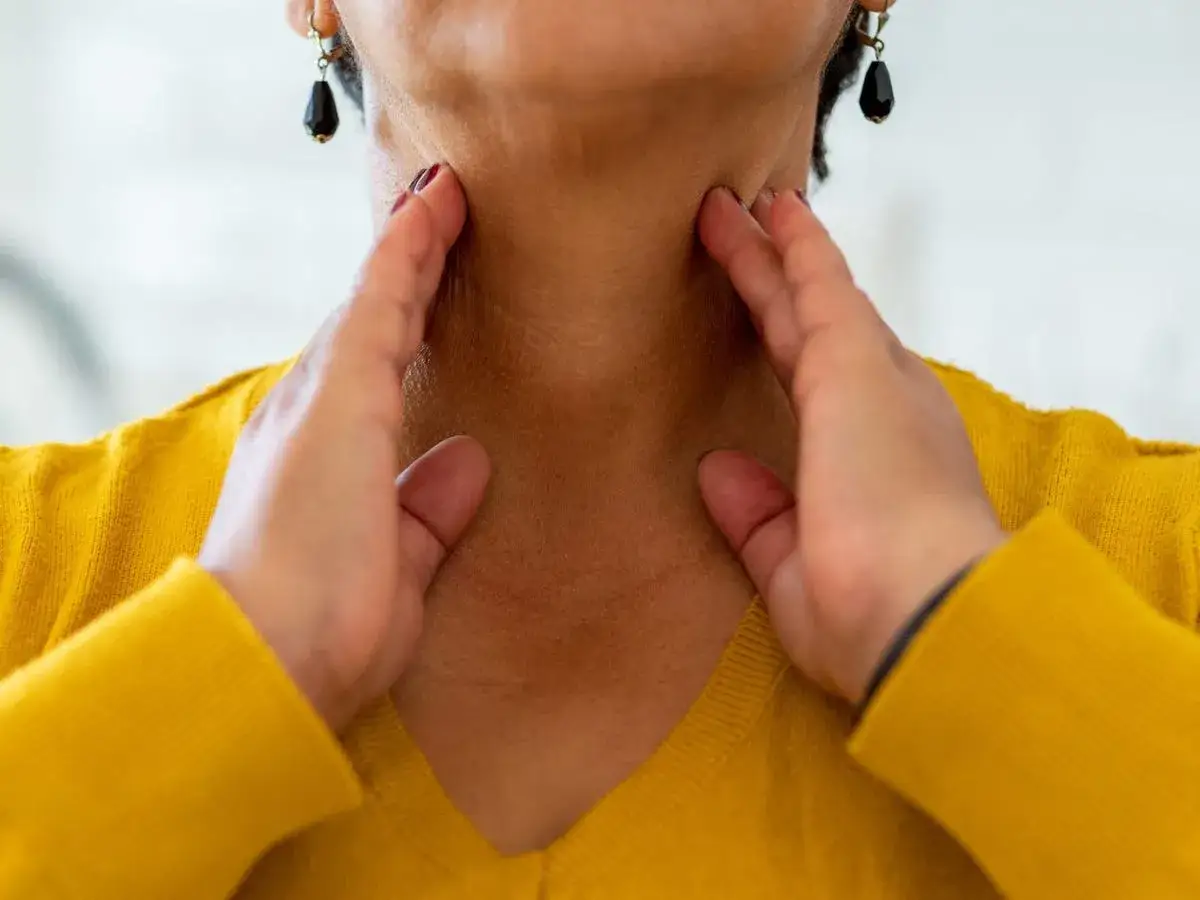 Kobieta dotyka szyi, odczuwając ostry b&oacute;l gardła przy przełykaniu bez gorączki.