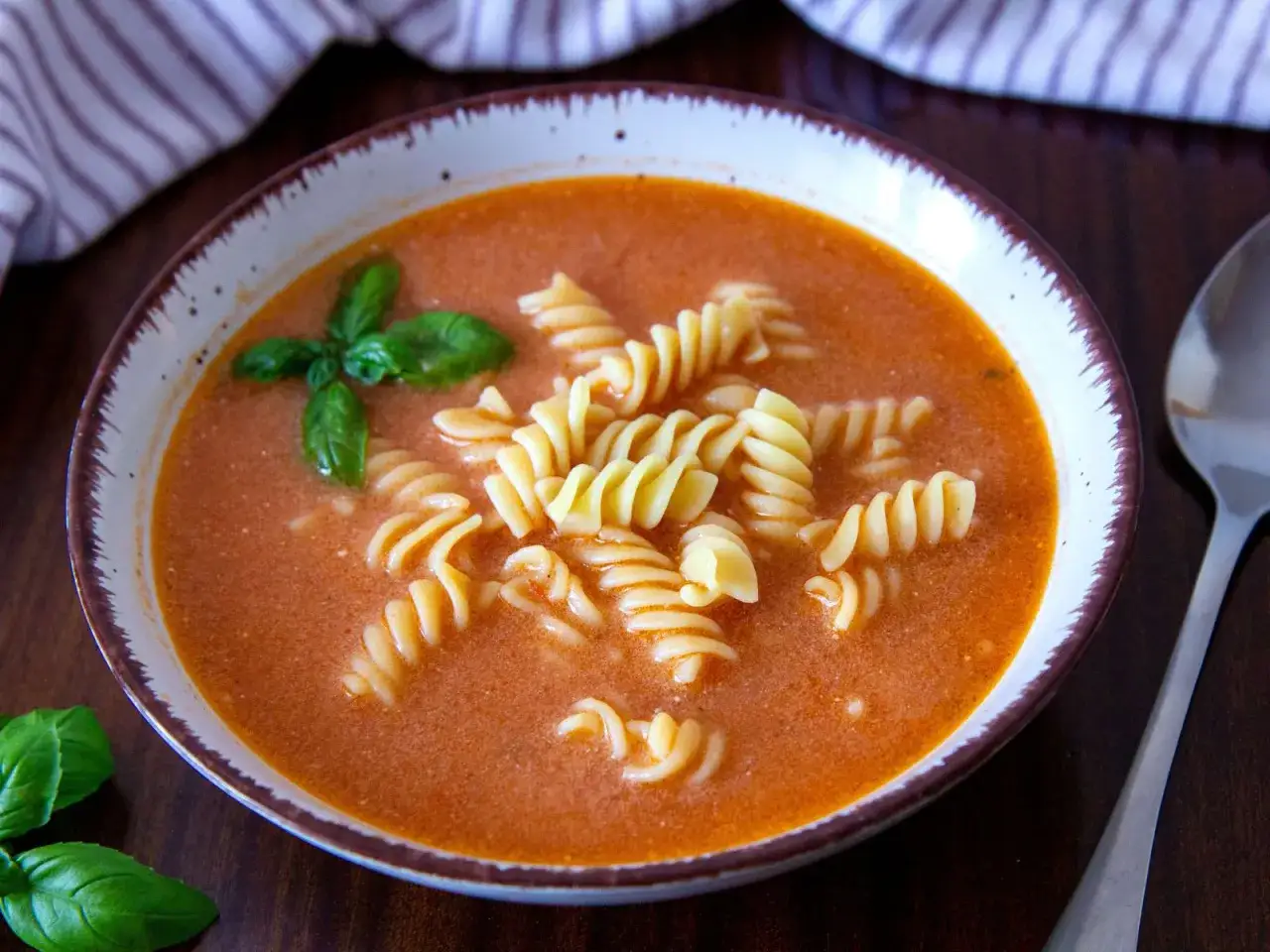Zupa pomidorowa z makaronem fusilli, ozdobiona bazylią. Idealna proporcja: ile koncentratu pomidorowego na litr wody?