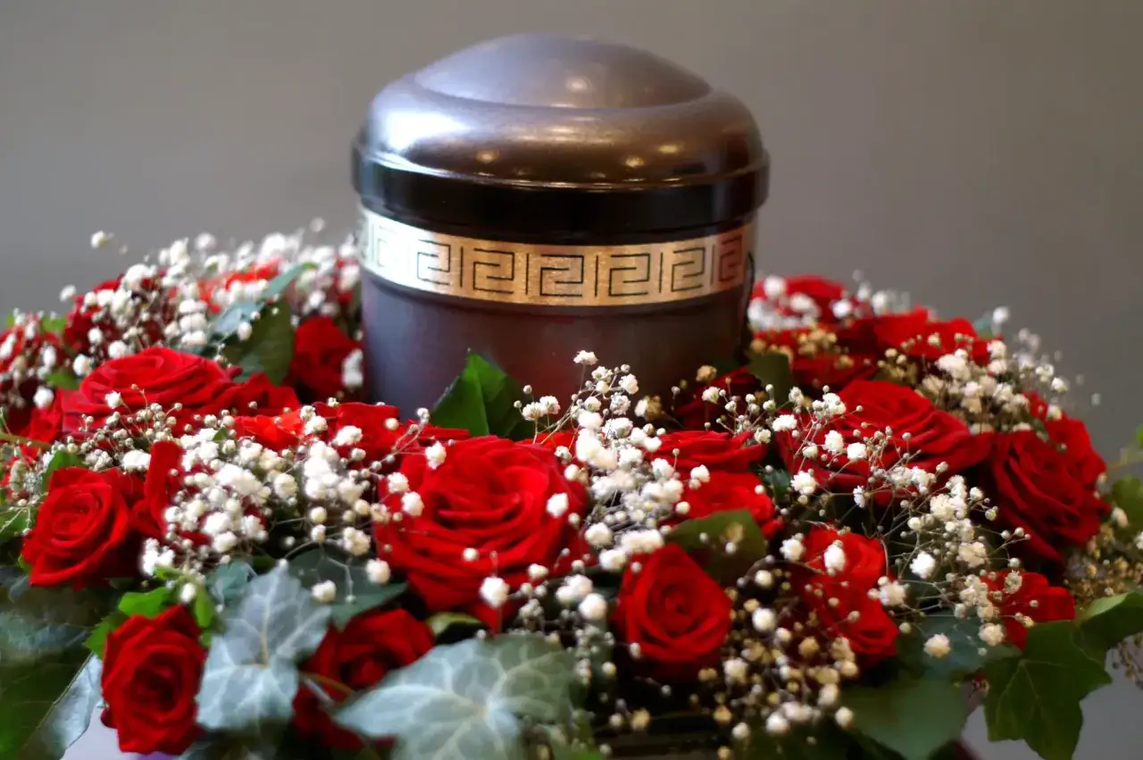 Urna z prochami otoczona czerwonymi różami i gipsówką. Czy kremacja jest grzechem? Pytanie to budzi wiele emocji.