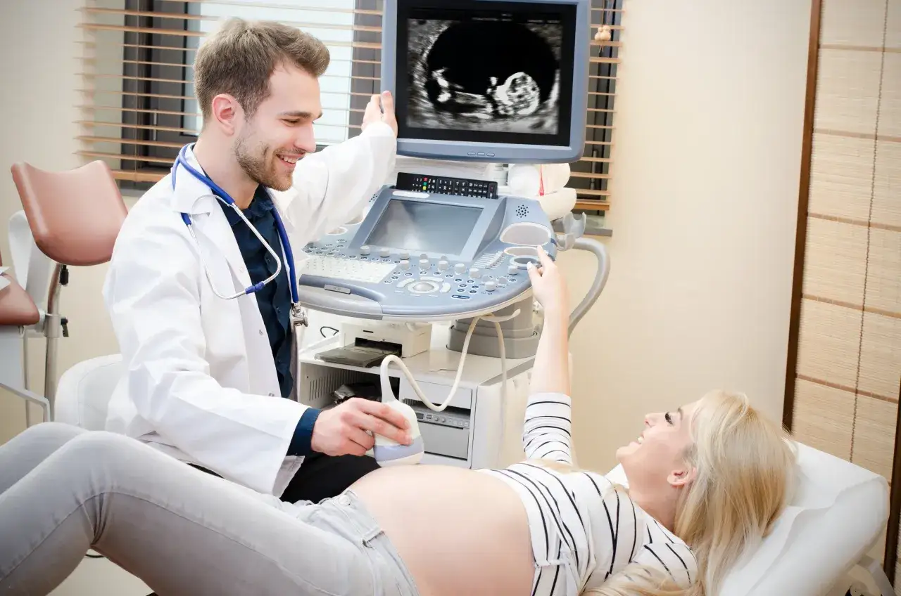 Lekarz wykonuje badania prenatalne, pokazując przyszłej mamie obraz USG. Dowiedz się, jak się przygotować do wizyty.