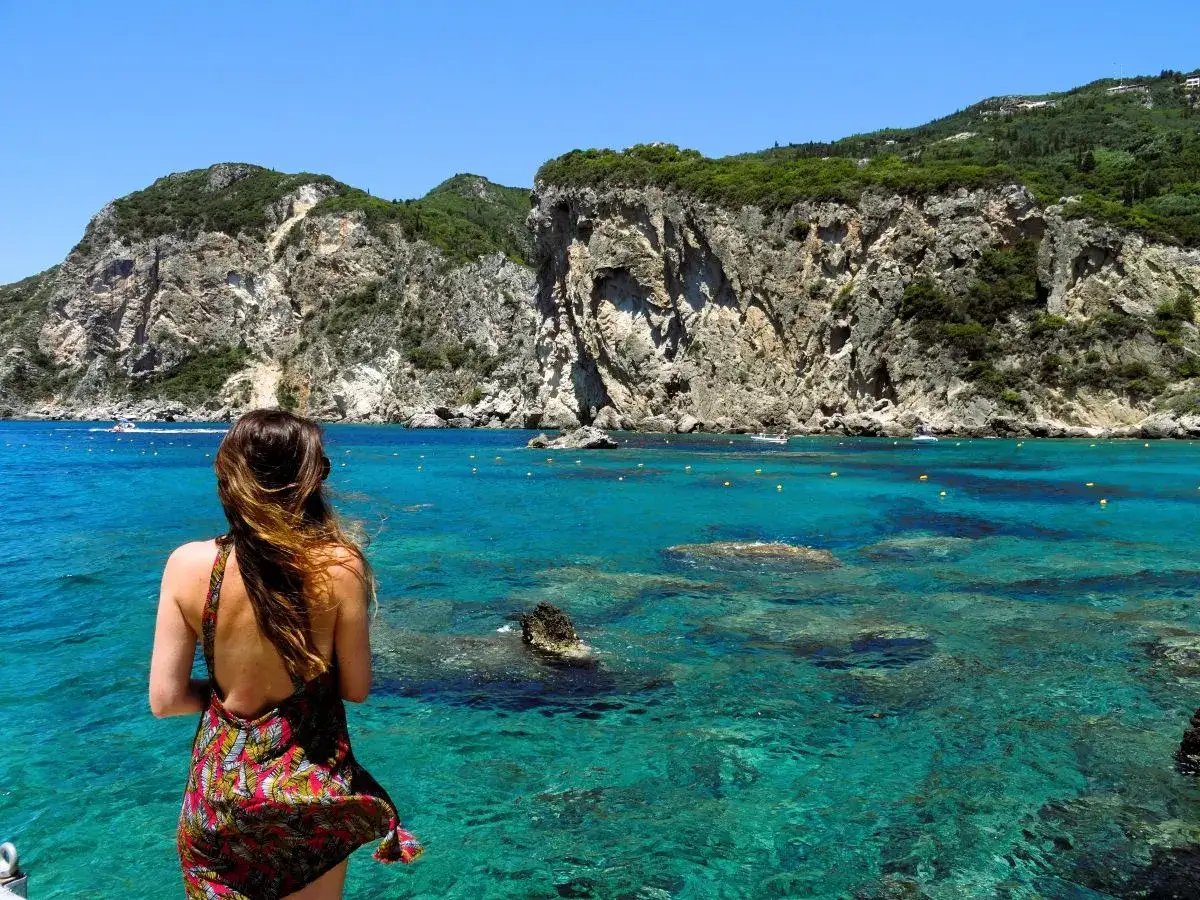 Kobieta podziwia turkusowe morze i skaliste klify na Korfu. Warto sprawdzić korfu ceny, by zaplanować taki widok.