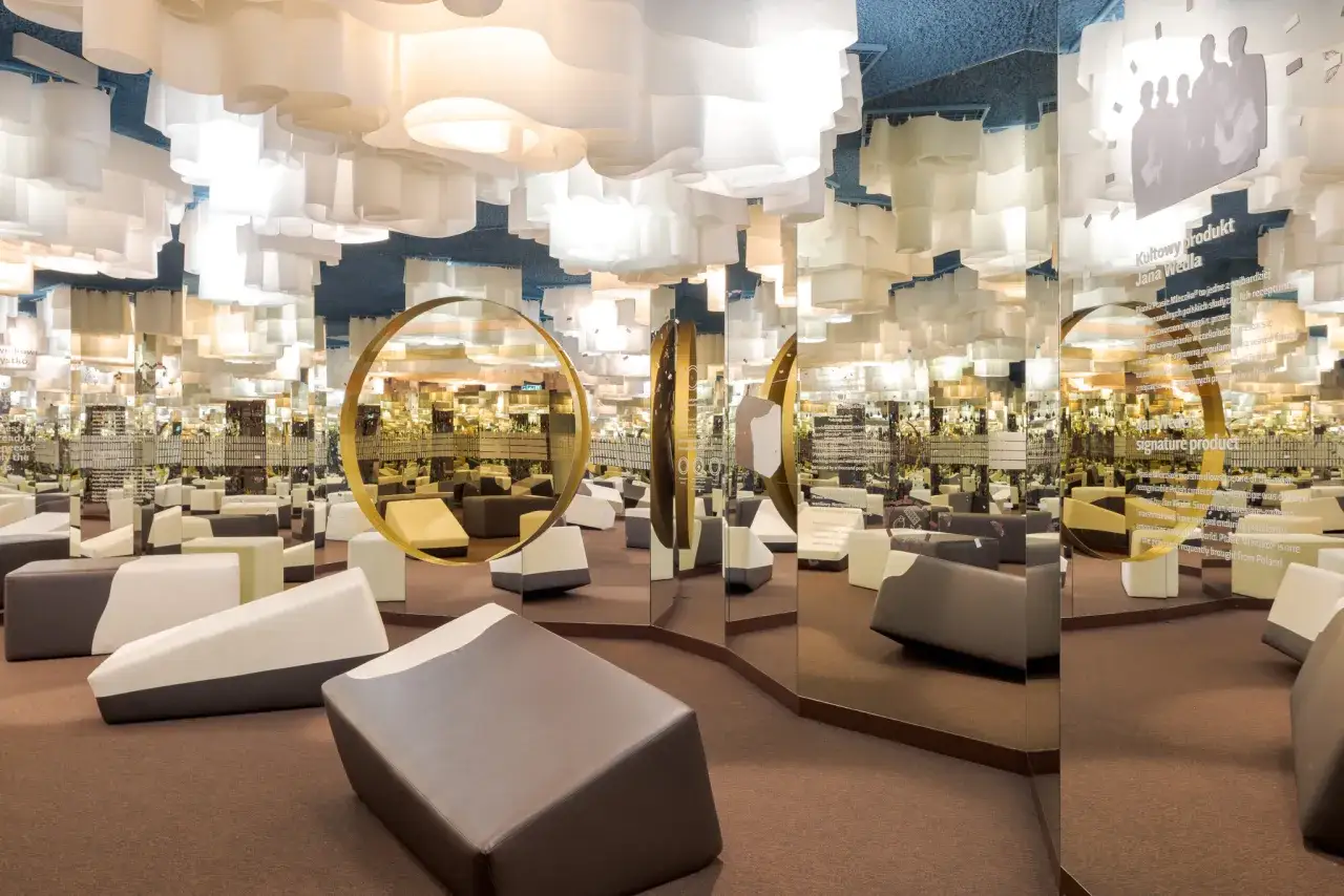 Wnętrze Muzeum Czekolady Warszawa z lustrzanymi ścianami, białymi, falującymi lampami i wygodnymi siedziskami.