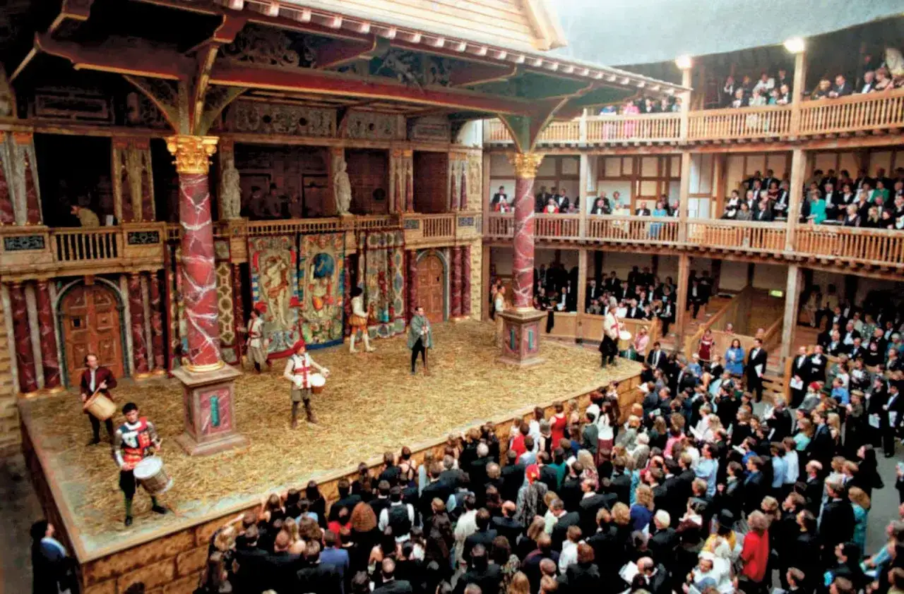 Scena teatralna z widownią, gdzie aktorzy w strojach z epoki odgrywają scenę, odzwierciedlając motyw theatrum mundi.