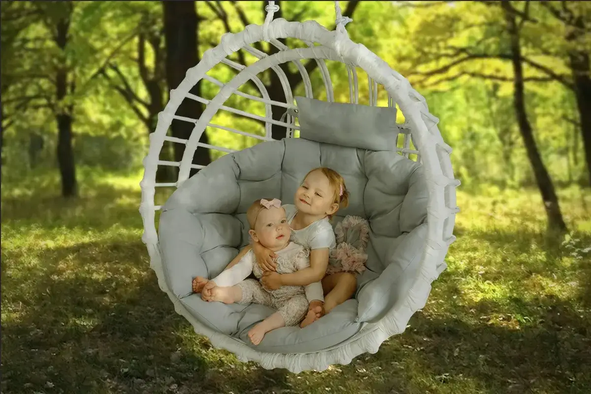 Dwie siostry przytulają się w huśtawce przypominającej biały kokon, otoczone zielenią lasu.