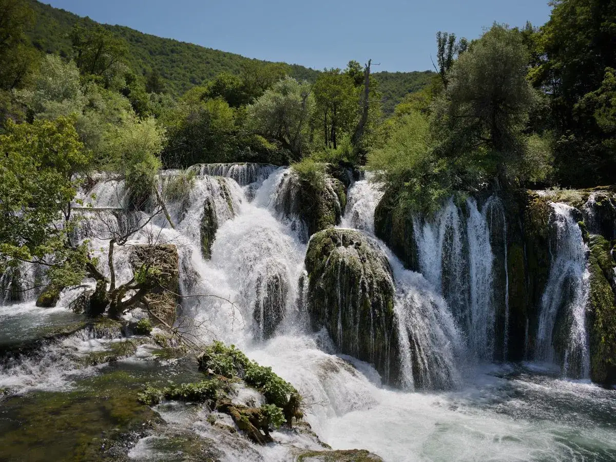 Wodospady w parku narodowym Una, kaskady wody spływającej po omszałych skałach, otoczone bujną zielenią.
