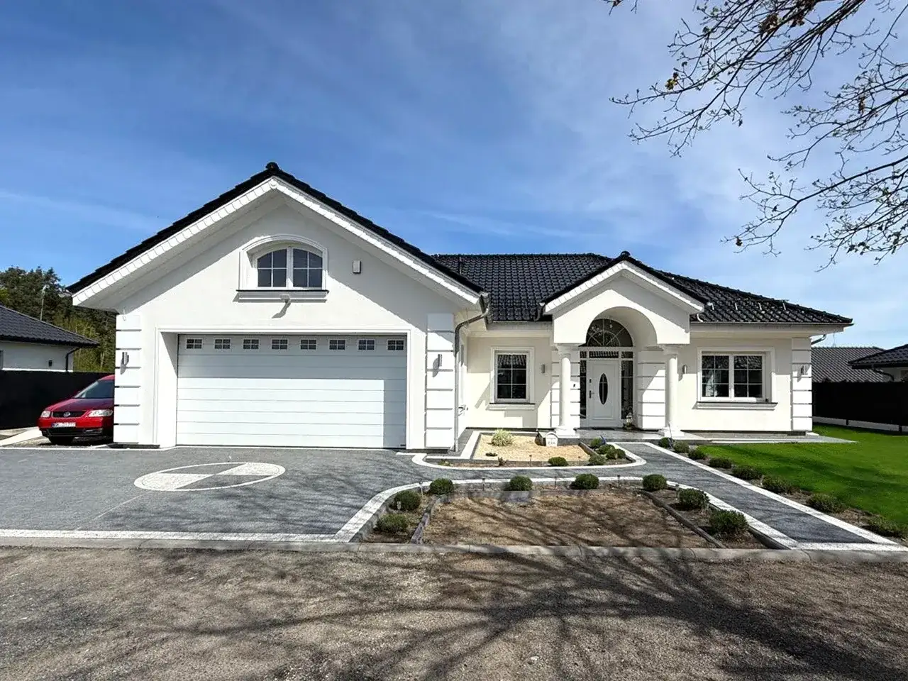 Nowoczesny dom z biało grafitową elewacją, czarnym dachem i podjazdem z kostki. Biała brama garażowa i drzwi wejściowe.