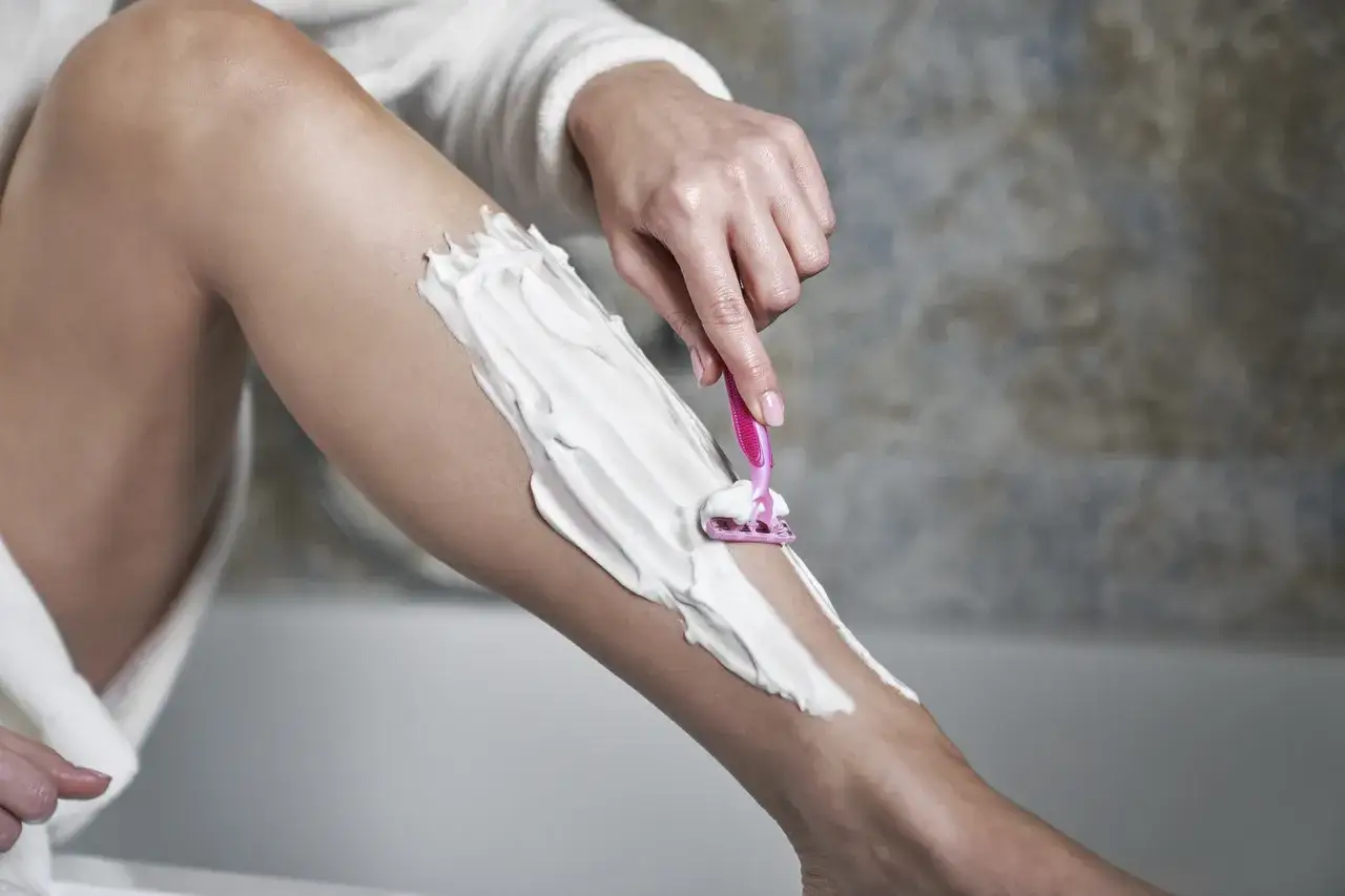 Kobieta goli nogi pianką i maszynką. Pokazany proces, jak ogolić nogi, by były gładkie.