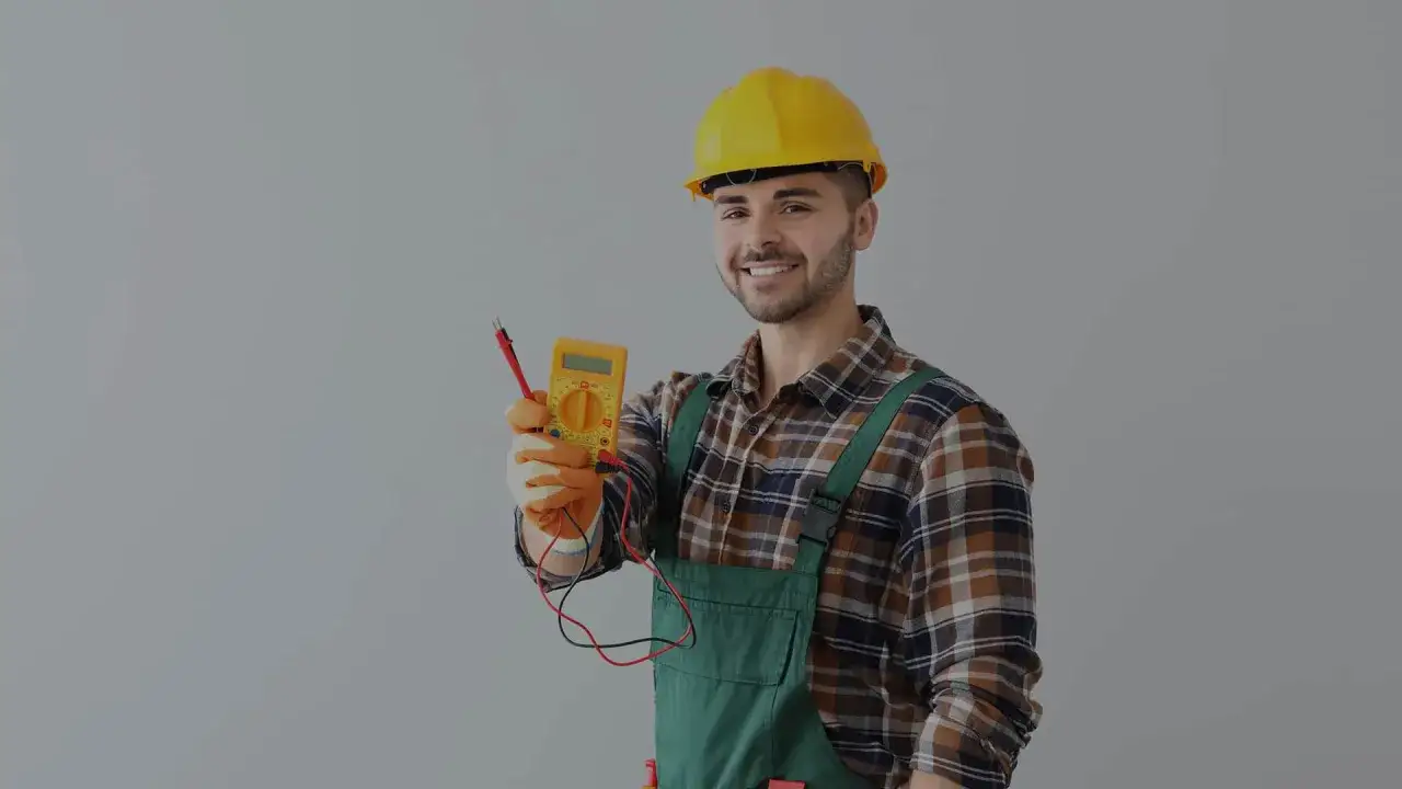 Uśmiechnięty elektryk w żółtym kasku trzyma miernik. Dowiedz się, ile kosztuje przegląd instalacji elektrycznej.