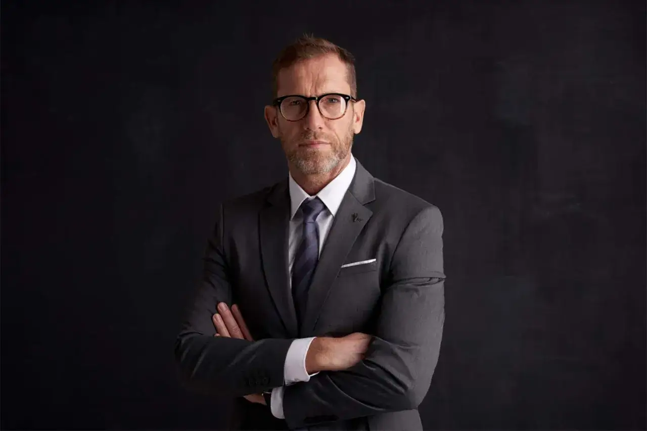 Elegancki mężczyzna w garniturze i okularach, z rękami skrzyżowanymi na piersi. Idealny do materiał&oacute;w promocyjnych dla firm fotograficznych.