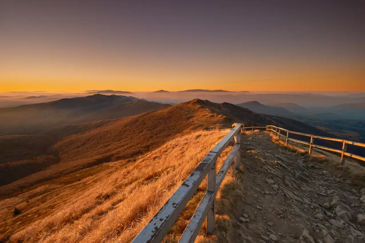Zach&oacute;d słońca nad pasmem g&oacute;rskim, gdzie szlak czerwony co oznacza drogę przez malownicze połoniny.