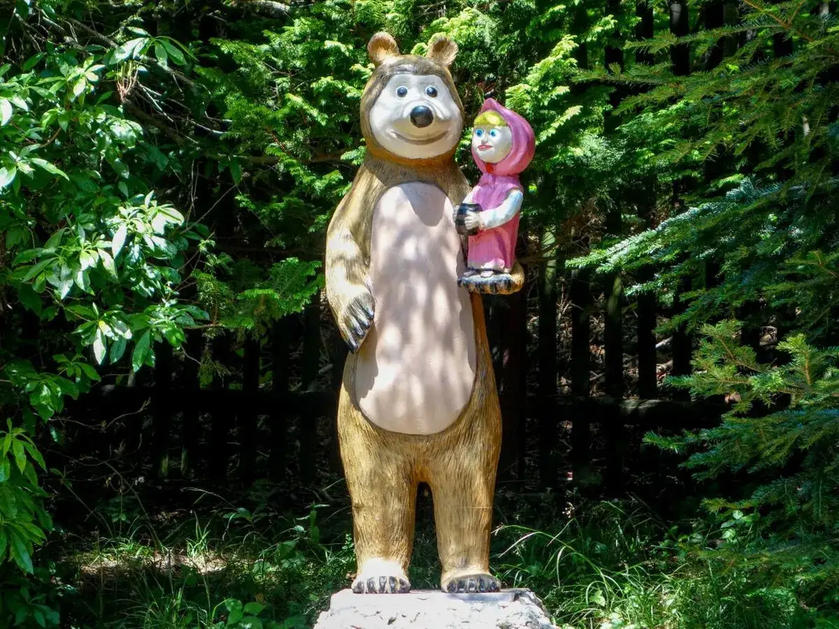 Miś i Masza w Ogrodzie Bajek Międzyg&oacute;rze. Figurki z bajki o Misiu i Maszy, stojące wśr&oacute;d zieleni.