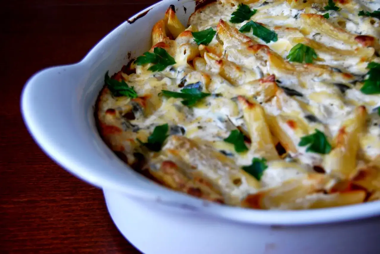 Pyszna zapiekanka makaronowa z kurczakiem, polana kremowym sosem i posypana natką pietruszki, prosto z piekarnika.