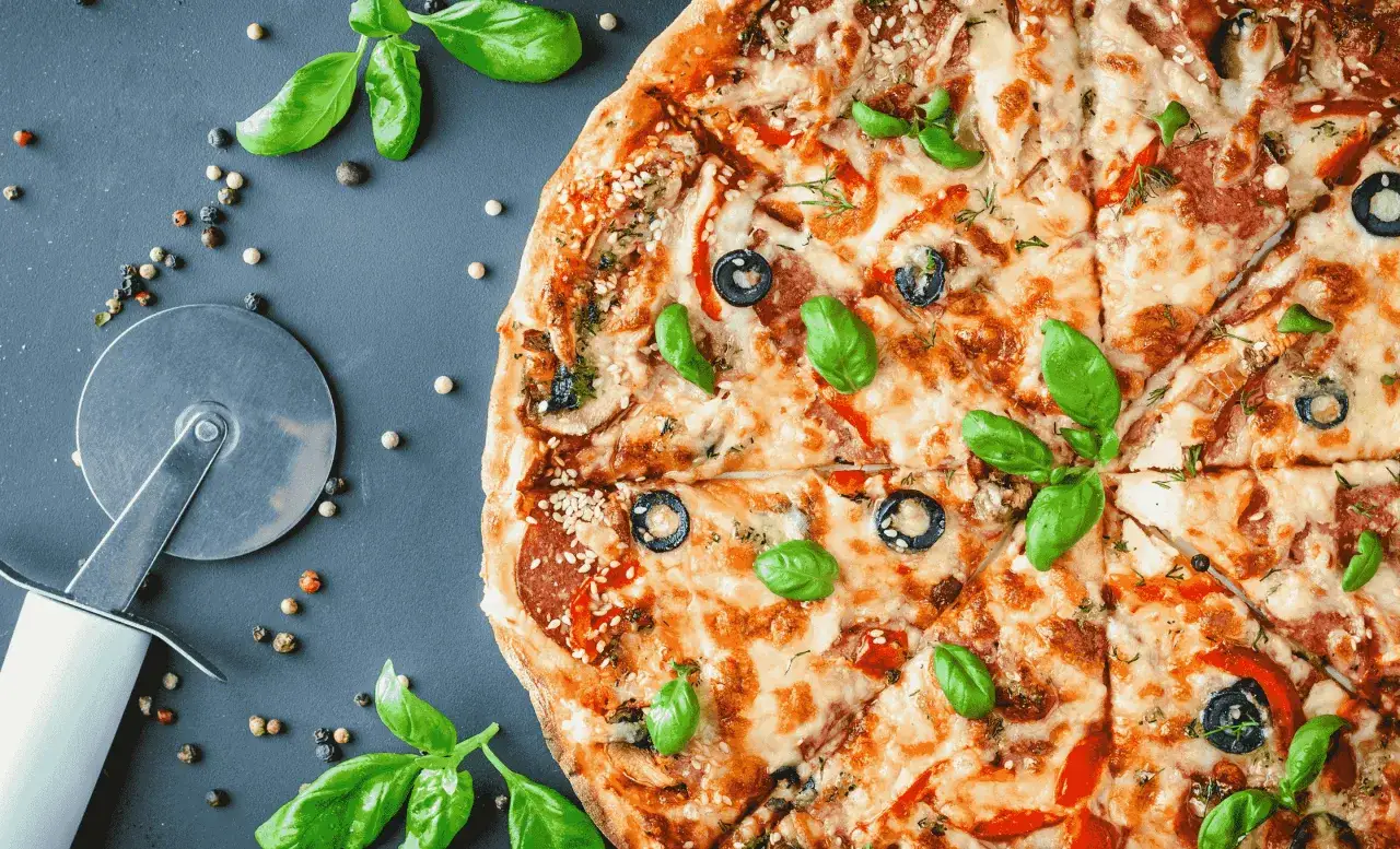 Pyszna pizza z oliwkami i bazylią, idealna na pytanie: gdzie zjeść w Krynicy Morskiej? Obok krajalnica i kolorowy pieprz.