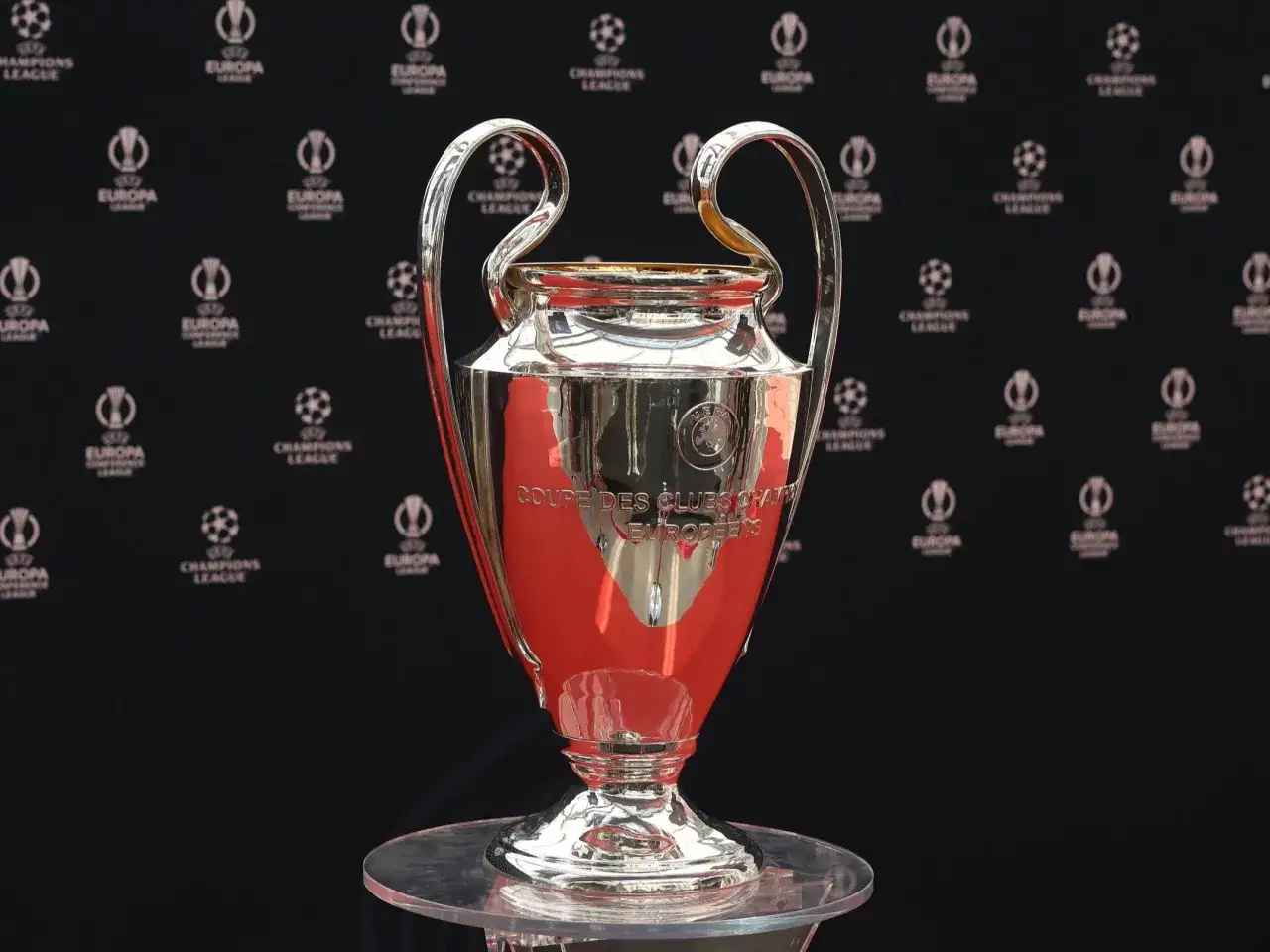 Trofeum Ligi Mistrzów błyszczy na tle logotypów UEFA. Gdzie oglądać mecze? Sprawdź w swojej telewizji!