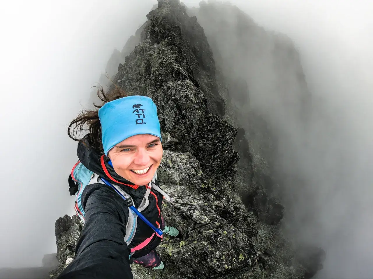 Uśmiechnięta turystka na grani, mgła otula skaliste szczyty. To jej droga, martina w chmurach.