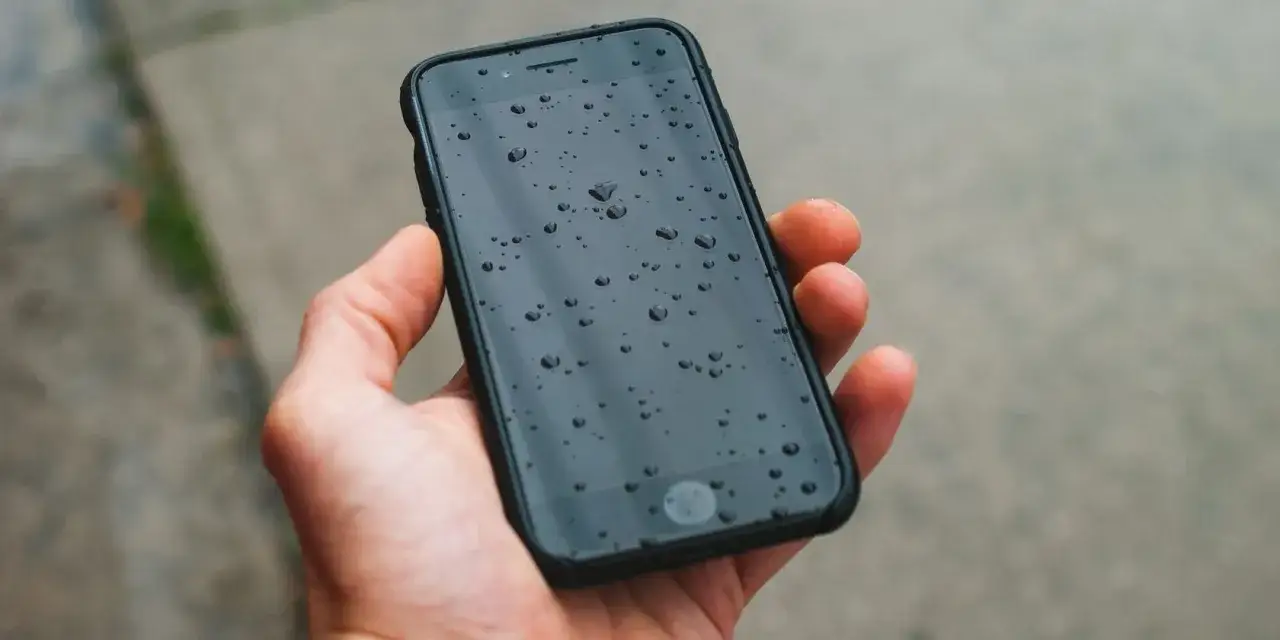 Dłoń trzyma smartfon z kropelkami wody na ekranie. Dzięki powłoce oleofobowej woda nie rozlewa się, lecz tworzy małe kuleczki.