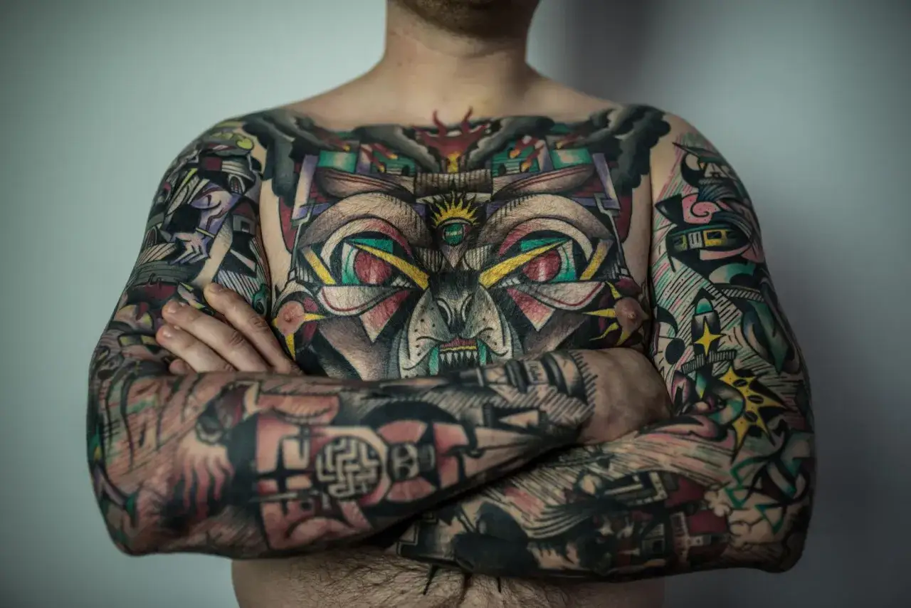 Mężczyzna z kolorowymi tatuażami na klatce piersiowej i ramionach. Czy prawnicy mogą mieć tatuaże? Ten obraz pokazuje, że sztuka ciała nie wyklucza żadnego zawodu.