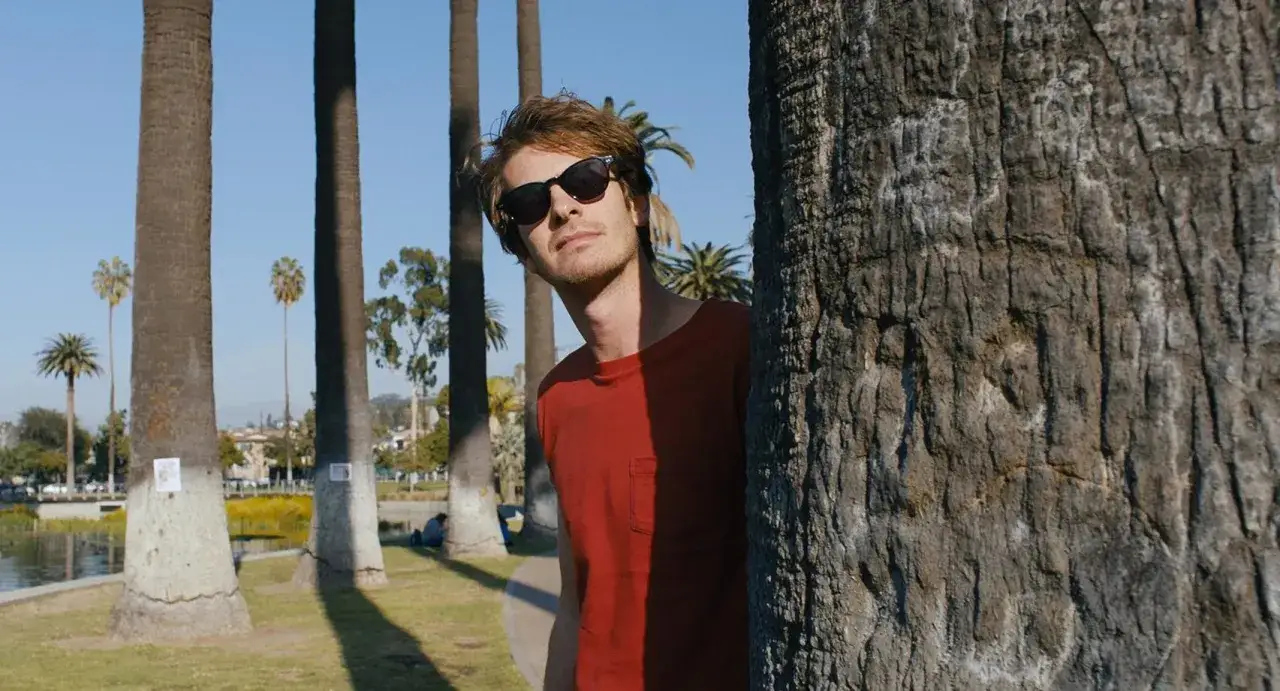 Mężczyzna w okularach przeciwsłonecznych i czerwonej koszulce ukrywa się za drzewem, jakby odkrywał tajemnice Silver Lake.