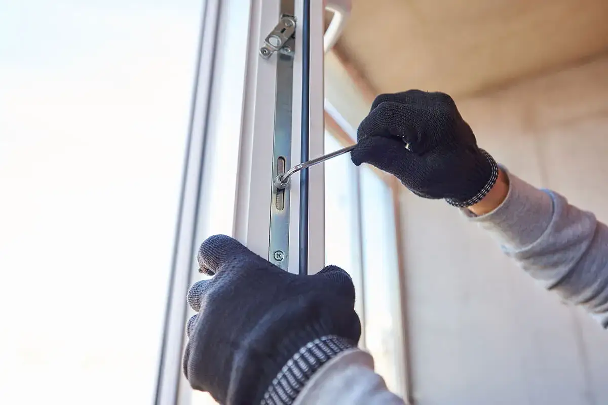 Ręce w rękawiczkach dokonują regulacji drzwi balkonowych, dokręcając śrubę kluczem.