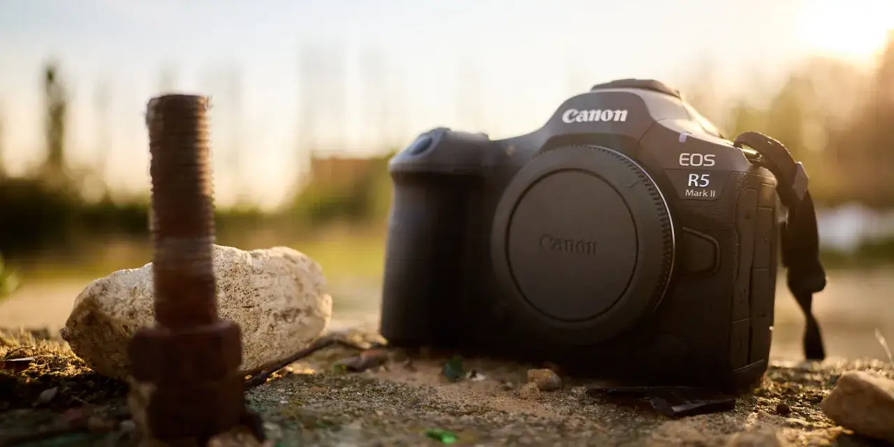 Canon R5 Mark II w teście. Aparat leży na kamieniu obok zardzewiałego śrubu.
