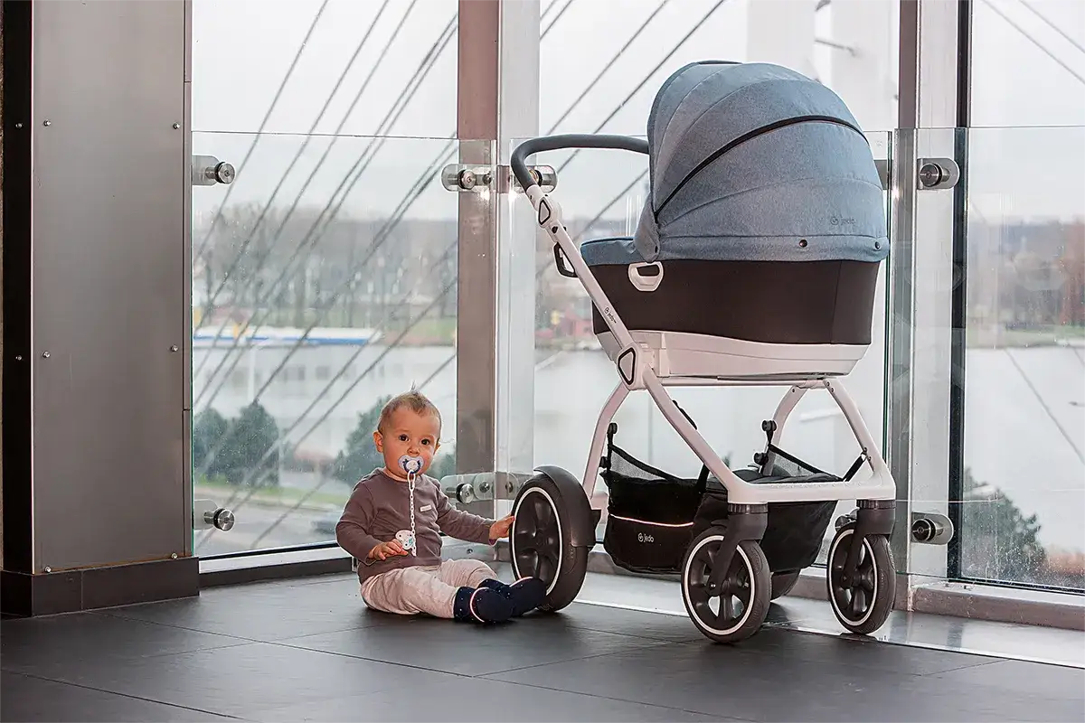 Maluch z smoczkiem obok nowoczesnej gondoli, kt&oacute;ra posłuży do jakiego wieku?