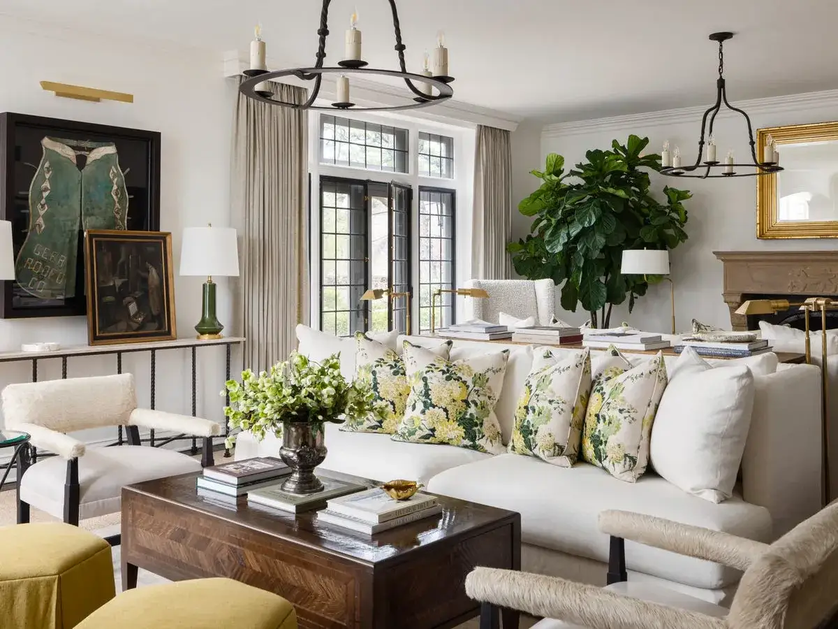 Oświetlenie salonu inspiracje: elegancki żyrandol i kinkiety tworzą przytulną atmosferę. Wygodna sofa z poduszkami w kwiaty.