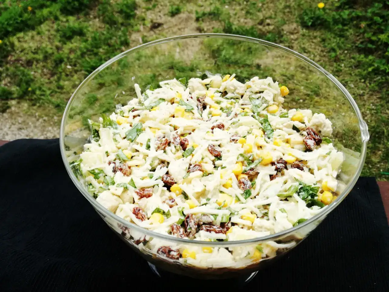 Pyszna pasta z gotowanego kurczaka z kukurydzą, rodzynkami i serem, podana w szklanej misie na tle zieleni.