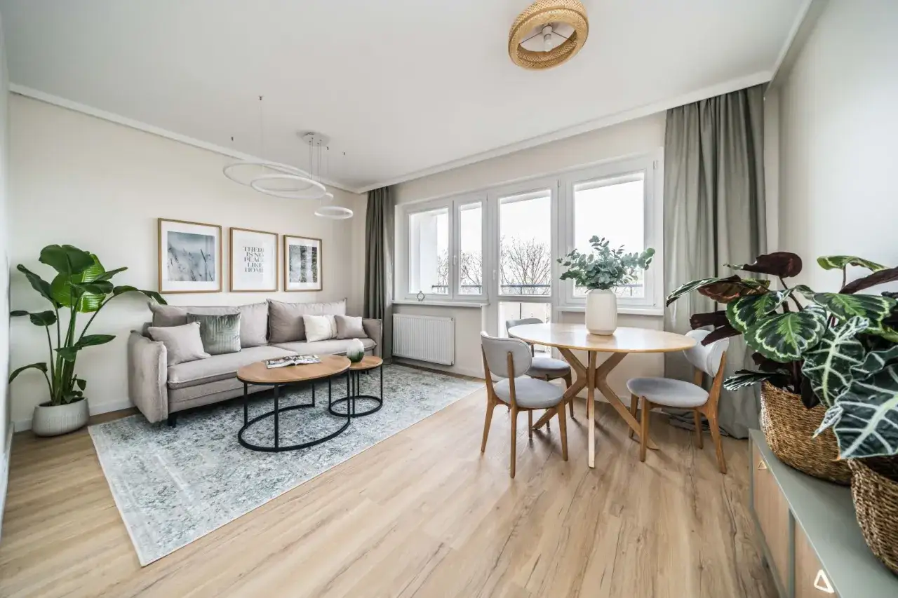 Przytulne, nowoczesne mieszkanie w bloku. Jasny salon z sofą, stolikami kawowymi, jadalnią i roślinami.