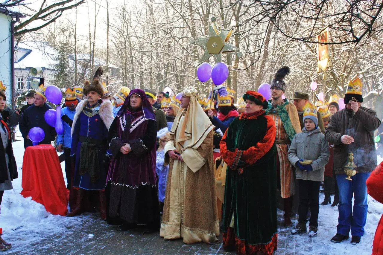 Grupa ludzi w barwnych strojach, z balonami i gwiazdą, świętuje z narodzenia pana.