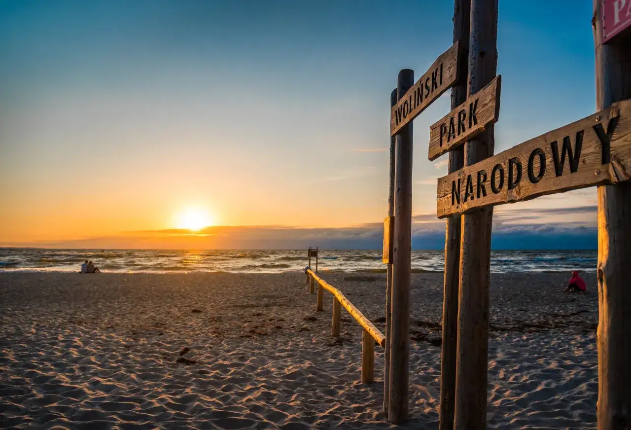 Zachód słońca na plaży, gdzie tablica informuje o Wolińskim Parku Narodowym. Czy Polska ma jakieś wyspy? Tak, a ta jest jedną z nich.