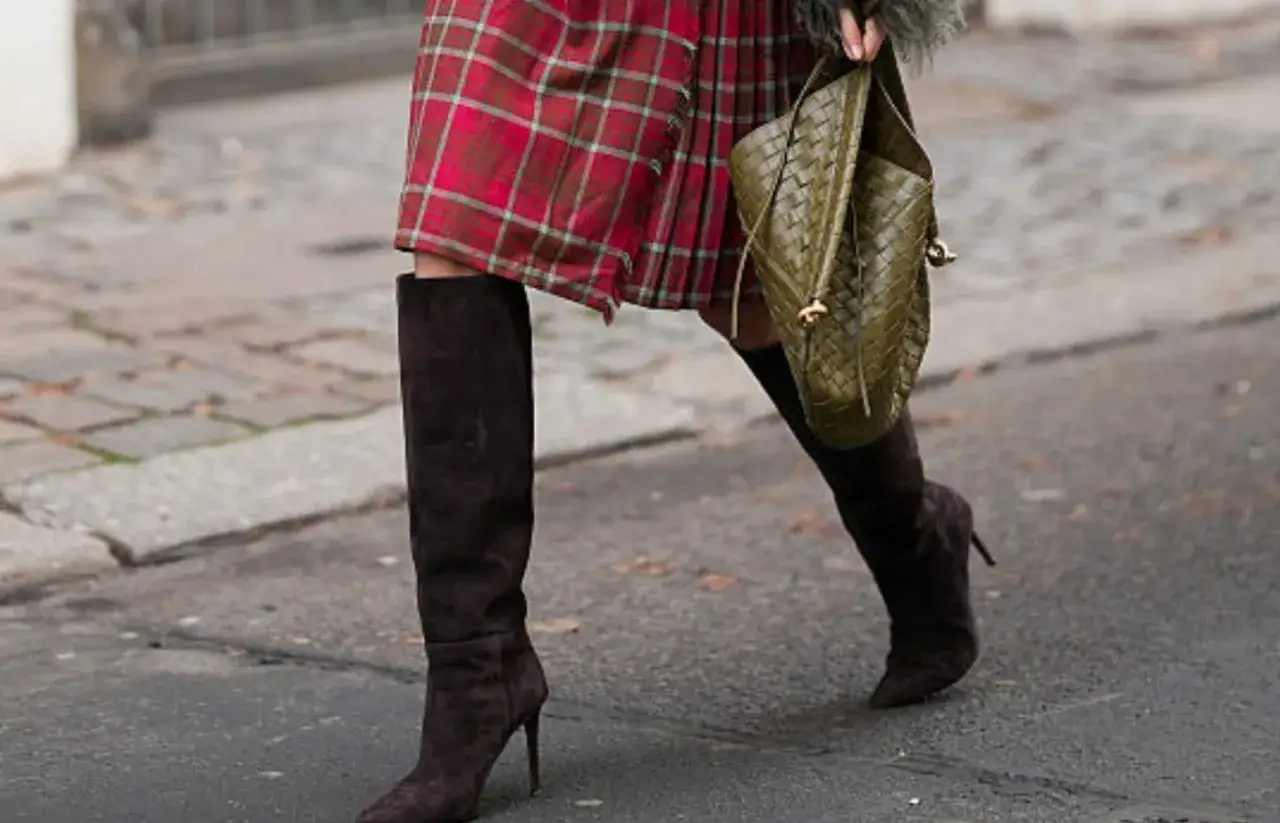 Eleganckie stylizacje ze sp&oacute;dnicą: czerwona sp&oacute;dnica w kratę, wysokie brązowe kozaki i zielona torebka.