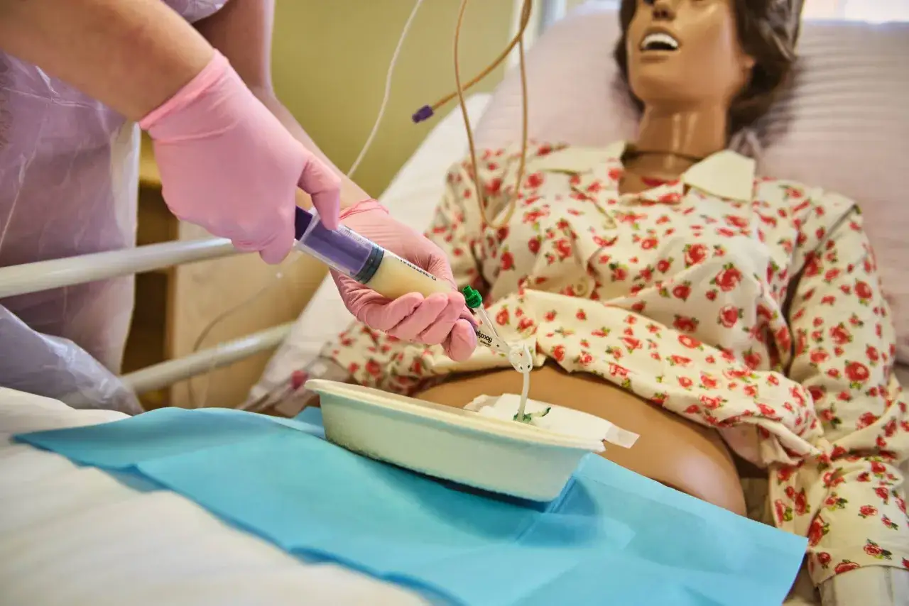 Opiekun medyczny w szpitalu podaje płyn przez sondę żołądkową za pomocą strzykawki.