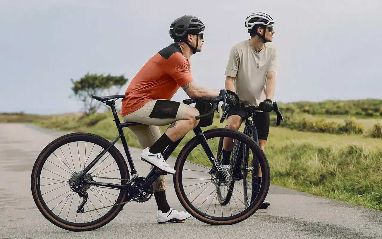 Dwóch kolarzy na rowerach typu gravel odpoczywa na poboczu drogi, podziwiając krajobraz.