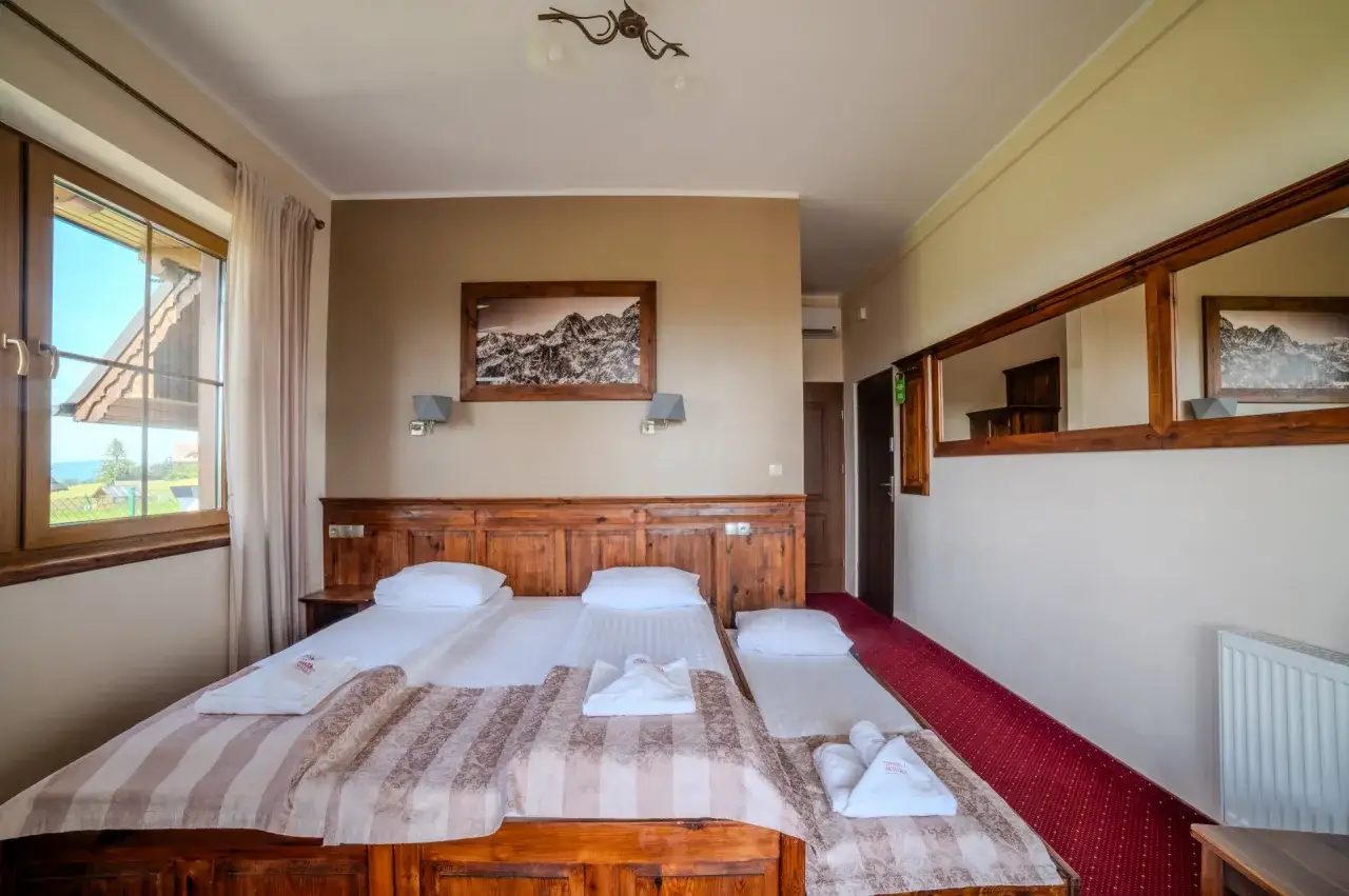 Pokój z trzema łóżkami, ozdobiony motywami górskimi, jak szarotka bukowina tatrzańska. Wygodne ręczniki i szlafroki czekają na gości.