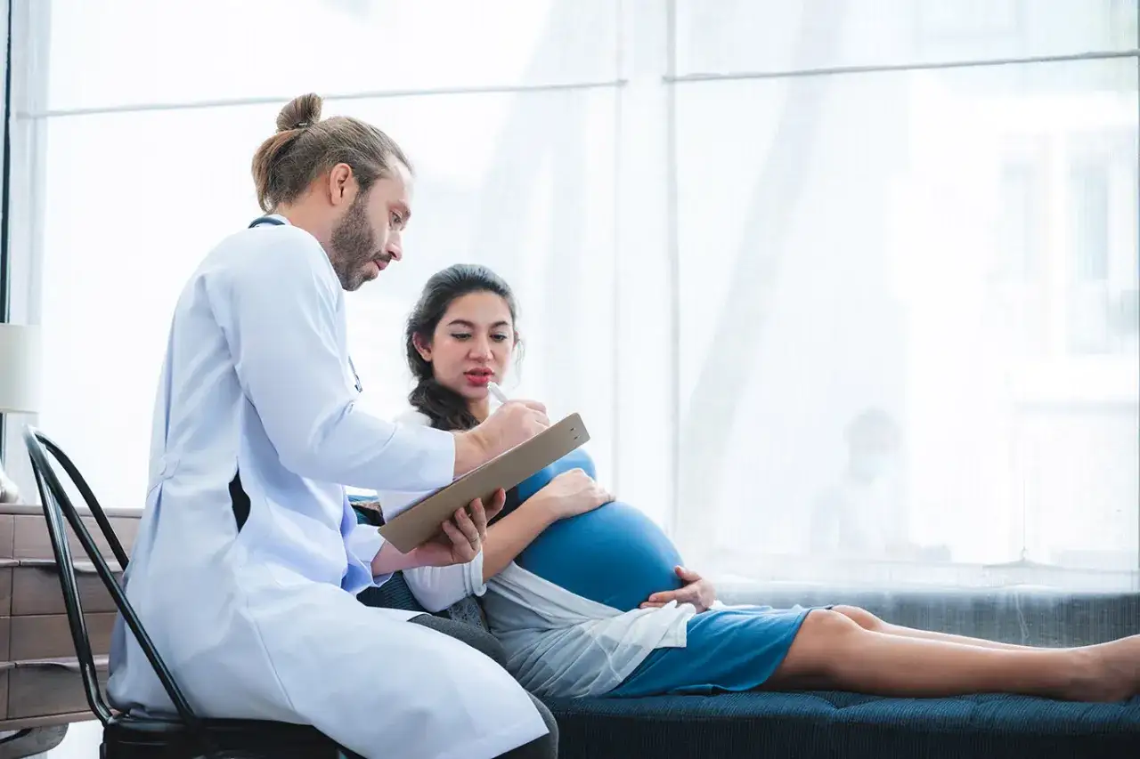 Lekarz rozmawia z ciężarną o lewatywie przed porodem. Kobieta trzyma się za brzuch.